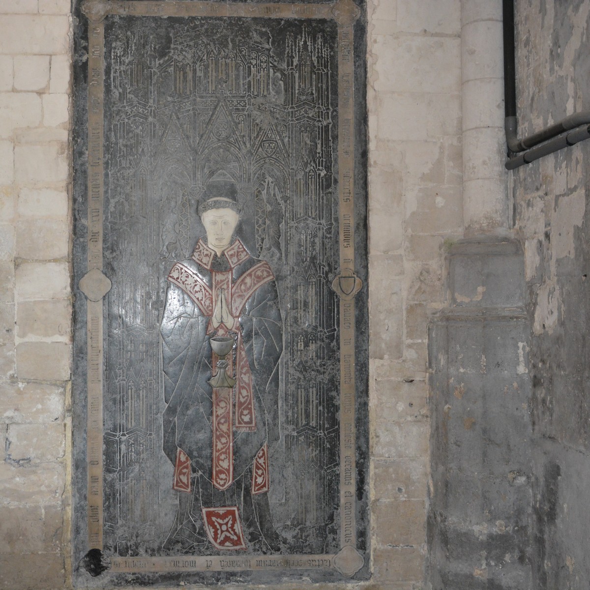 Cathédrale de Saint-Omer  -  Sur le côté et encastrée dans la muraille, on voit une merveilleuse pierre tombale sur laquelle est gravée un riche portique gothique. Elle porte des incrustations de marbre blanc, de cuivre et d'une pierre jaunâtre relevée de vermillon. 
Aux quatre angles se trouvent les symboles des Évangélistes dans les quatre fouilles. Une  inscription  avec les armes  du  défunt  rappelle le	nom du chanoine Simon Bocheux, doyen du Chapitre de Saint-Omer en 1423 et rappelé à Dieu en 1462.