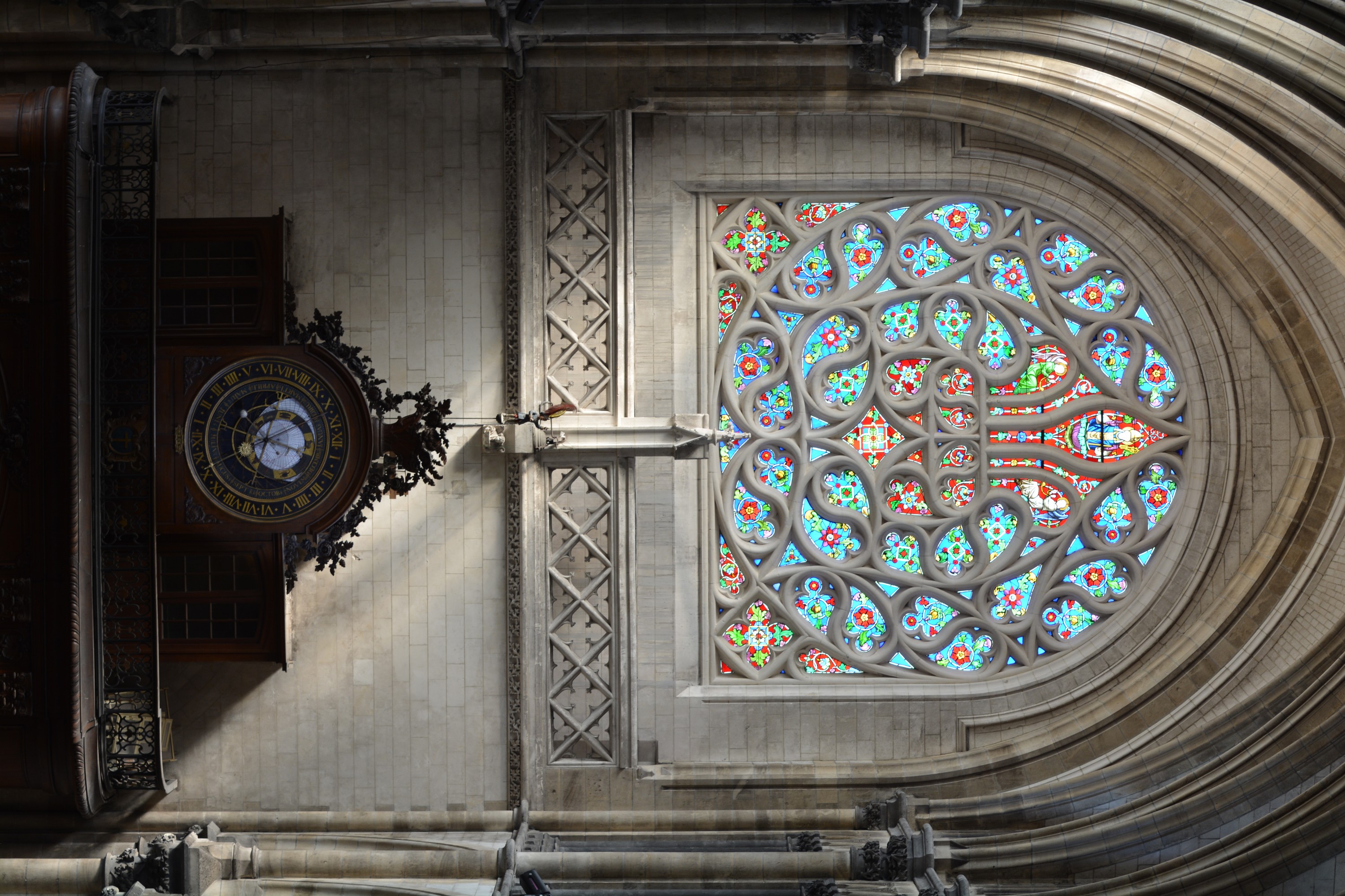 Cathédrale de Saint-Omer | rosace Nord | Rose à remplage supérieur en forme de fleur de lys. Deux écoinçons dans le bas forment une base horizontale. Verre à dominante rouge. Tout autour, multiples mouchettes entremêlées, à dominante bleue. Quadrilobes aux angles inférieurs sur pointe carrée.