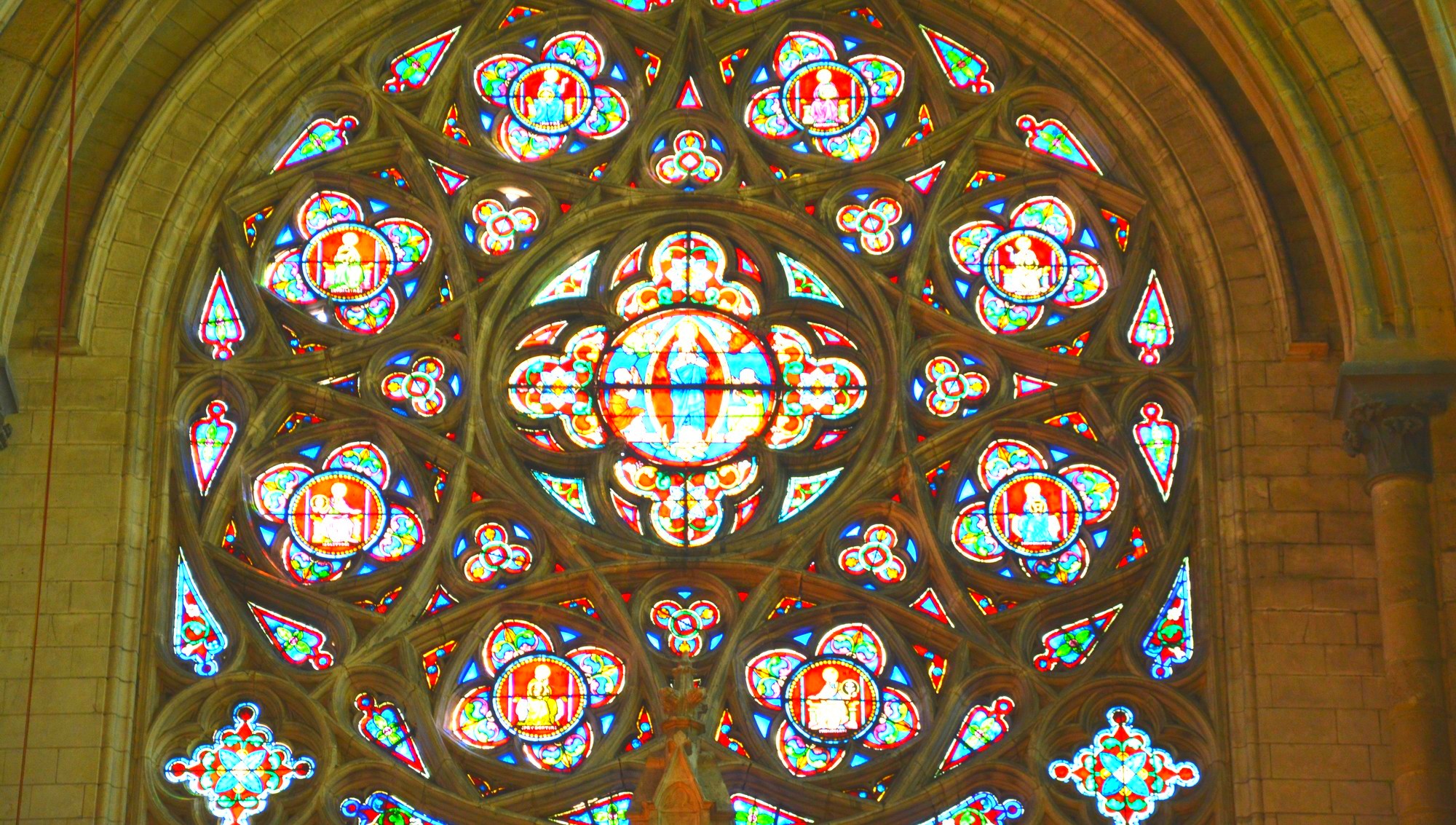 Cathédrale de Saint-Omer | rosace Sud | Rose à remplage central circulaire, encadré de huit grands quadrilobes et huits petits. Deux écoinçons dans le bas forment une base horizontale. Verre à dominante rouge et bleue. Aux extrémités inférieures, deux grands quadrilobes. Les espaces intermédiaires sont remplis par des mouchettes et de très petits écoinçons.